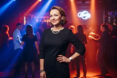 Elegancka kobieta w czarnej sukience, idealna inspiracja, jak się ubrać na dyskotekę po 40. Taniec w blasku świateł.