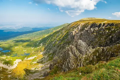 Widok na skaliste zbocze i zieloną dolinę z jeziorami. Śnieżne kotły ukazują swoją wysokość w majestatycznym krajobrazie.