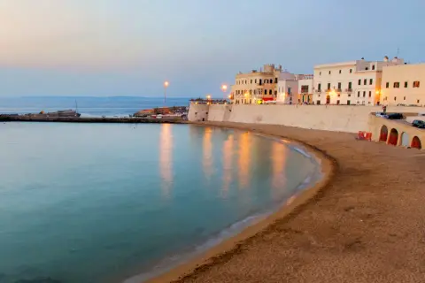 La costa di un paese vicino a Lecce al tramonto, con edifici bianchi, una spiaggia sabbiosa e il mare calmo.