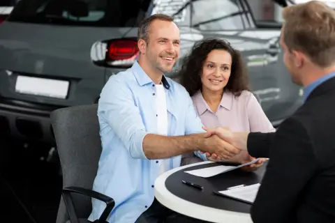 Un couple heureux finalise un accord de rachat de franchise avec un concessionnaire automobile, scellant leur nouvelle acquisition par une poignée de main.