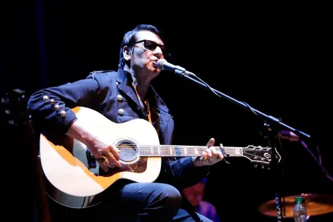 Artysta w okularach przeciwsłonecznych gra na gitarze i śpiewa. Nawet gdy boli mnie głowa i nie mogę spać, muzyka daje ukojenie.
