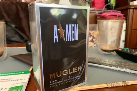 Pudełko perfum Mugler A*Men, zapach dla mężczyzny, w folii, na stole obok szklanki.