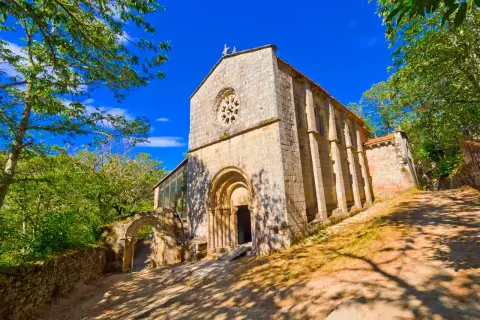 Monasterio de Santa Cristina de Ribas de Sil, una joya románica rodeada de exuberante vegetación bajo un cielo azul intenso.