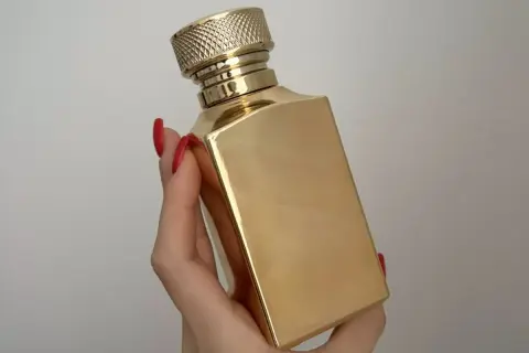 Złota butelka perfum Tiziana Terenzi Kirke, trzymana w dłoni z czerwonymi paznokciami.