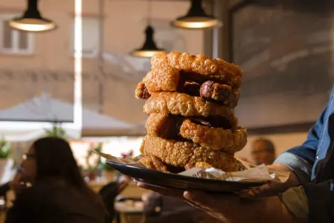 Torre de torrezno crujiente, ¡el mejor torrezno de Zaragoza! Servido en plato negro, listo para disfrutar.