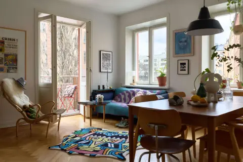 En ljus och färgstark lägenhet med 60-tals inredning. En blå soffa med mönstrat överkast, en trästol med fårskinn och en lekfull matta på parkettgolvet.