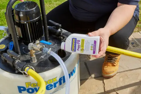 Osoba dodaje środek do czyszczenia instalacji co do urządzenia Fernox Powerflow.