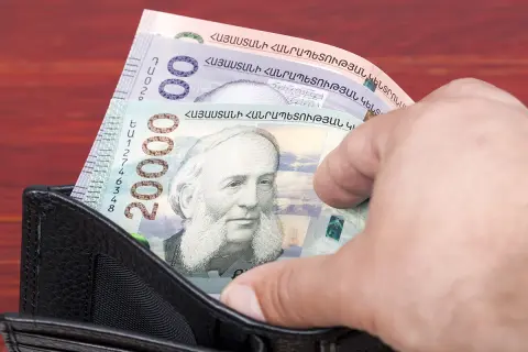 Dłoń wyciąga z portfela banknot 20000 dramów, waluta Armenii. Widoczne też inne banknoty.