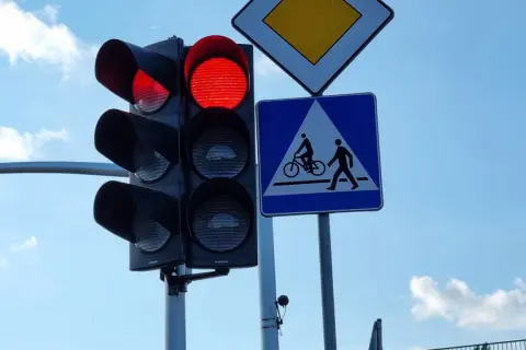 Czerwone światło na sygnalizatorze drogowym, obok znak d6 informujący o przejściu dla pieszych i rowerzystów.