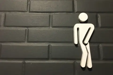 Biały symbol mężczyzny na ciemnej, ceglanej ścianie. Może symbolizować problemy z oddawaniem moczu, takie jak niskie ciśnienie moczu u mężczyzn.