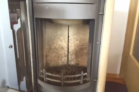Innenansicht eines Ofens mit sichtbaren Schamottsteinen, die von Ruß und Asche bedeckt sind.