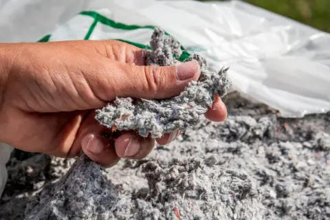 Dłoń trzyma grudkę celulozy, materiału używanego do ocieplenia domu.