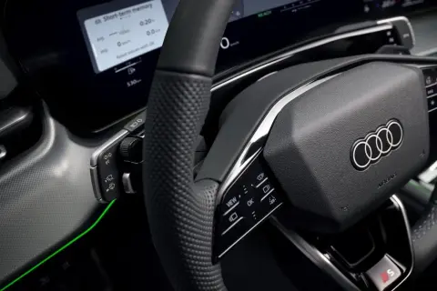 Wnętrze nowoczesnego samochodu Audi. Kierownica z przyciskami, ekran z informacjami o podróży i zielone podświetlenie. Czy to elektryczny samochód?