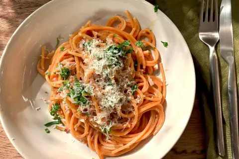 En tallrik med god pasta, toppad med riven ost och färska örter. En gaffel och kniv ligger bredvid.