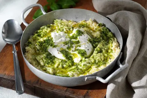 En skål med pasta som ser ut som ris, toppad med krämig burrata och grön pesto. En utsökt rätt som ser ut att vara gjord med kärlek.