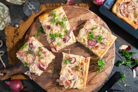 Saftiger Zwiebelkuchen vom Blech, belegt mit roten Zwiebeln und Speck, garniert mit Petersilie.