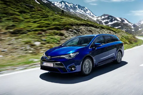 Niebieska Toyota Avensis T27 1.8 benzyna przemierza górską drogę, otoczona zielonymi zboczami i ośnieżonymi szczytami.
