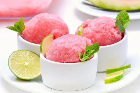 Orzeźwiający sorbet z arbuza w białych miseczkach, udekorowany listkami mięty i plasterkami limonki. Idealny na upalne dni.