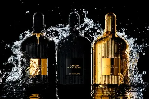 Trzy flakony perfum Tom Ford Black Orchid, w tym jeden złoty, otoczone wodnymi rozpryskami. Wyczuwalna nuta wanilii.