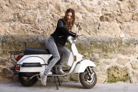 Joven con chaqueta de cuero y jeans sobre una scooter blanca, lista para el mantenimiento de su scooter 125.