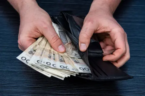 Dłonie trzymają portfel z polskimi banknotami. Czy wdowa może przejąć emeryturę po mężu? Pieniądze w portfelu.