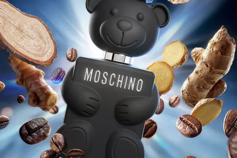 Czarny flakon Moschino Toy Boy w kształcie misia otoczony ziarnami kawy i imbirem.