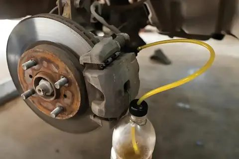 Proceso de purgar frenos: un tubo amarillo conecta la pinza de freno a una botella para extraer el líquido.