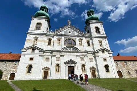 Majestatyczny klasztor Ojców Kamedułów na Bielanach z zielonymi kopułami wież, pod błękitnym niebem z chmurami.