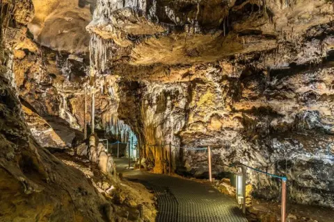 Interior de cuevas cerca de Madrid, con estalactitas y estalagmitas iluminadas, y un sendero metálico para visitantes.
