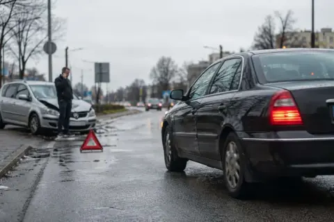 Wypadek drogowy. Mężczyzna rozmawia przez telefon obok uszkodzonego samochodu. Trójkąt ostrzegawczy na drodze. Sprawa dla ubezpieczyciela, regres ubezpieczeniowy.