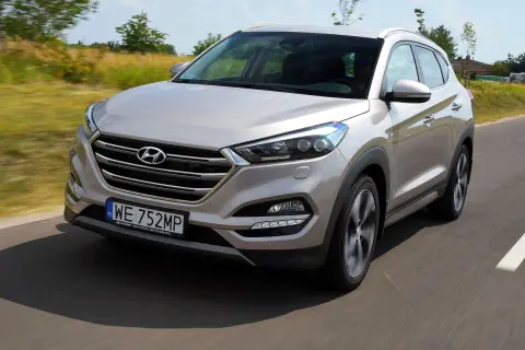 Srebrny Hyundai Tucson 2016 jedzie po drodze, otoczony zielenią.