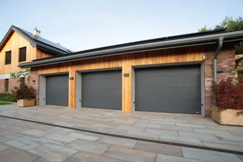 Tre moderna garageportar i mörkgrått framför ett hus med träfasad och tegelfasad.