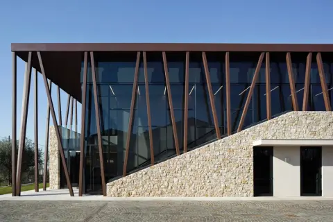 Edificio moderno con facciata in pietra e vetro, travi inclinate in metallo marrone. Un'architettura che evoca i valetti di Bardolino.