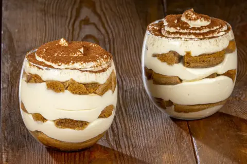 Due bicchieri di delizioso tiramisù senza uova, stratificato con crema e savoiardi, spolverato di cacao.