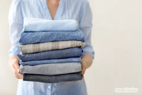 Ein Stapel frisch gewaschener Hemden in verschiedenen Blautönen und Mustern, gehalten von einer Person in einem hellblauen Hemd.