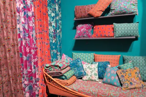Rideau **couleur corail** et coussins aux motifs floraux et paons, sur un banc en rotin.
