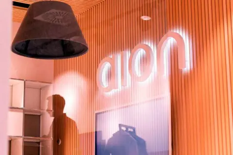 Jasne, oto propozycja:

Logo Aion Bank S.A. świeci na pomarańczowej ścianie. W tle widać cień postaci i regały.