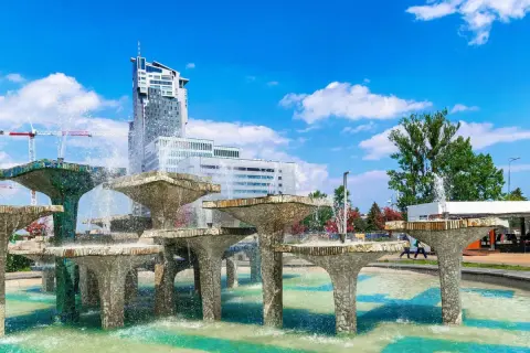 Fontanna z modernistycznymi budynkami w tle i błękitnym niebem.