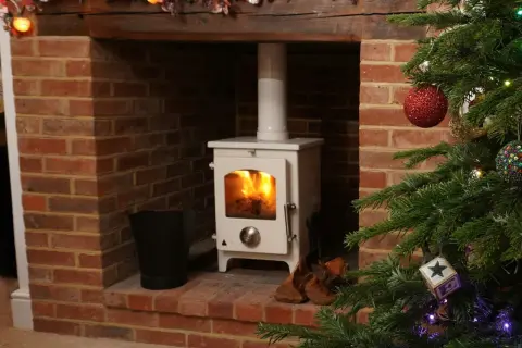 Poêle à pellets blanc dans une cheminée en briques, avec une cheminée décorée pour Noël. Le raccordement poêle à pellet sur cheminée est visible.