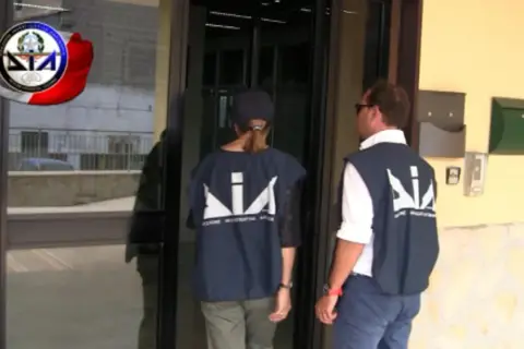 Agenti della DIA, Direzione Investigativa Antimafia, si avvicinano a un ingresso.