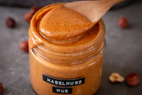 Cremiges Haselnussmus im Glas, bereit für leckere Rezepte mit Haselnussmus. Ein Holzlöffel schöpft die köstliche Masse.