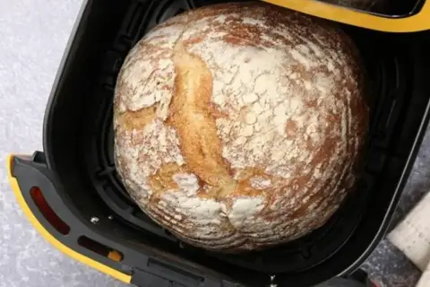 Chleb z airfryer, rumiany i lekko oprószony mąką, czeka na wyjęcie.