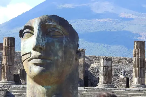 Pompeje: miasto grzechu. Monumentalna głowa rzeźby na tle ruin i Wezuwiusza.