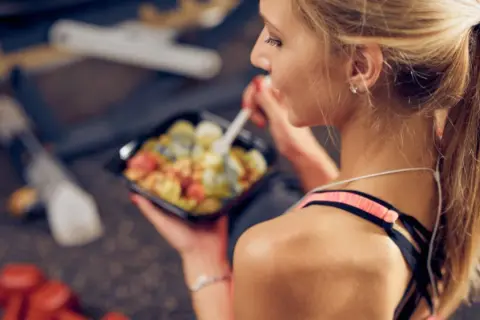 Junge Frau isst nach dem Sport eine gesunde Mahlzeit aus einer Plastikschale.