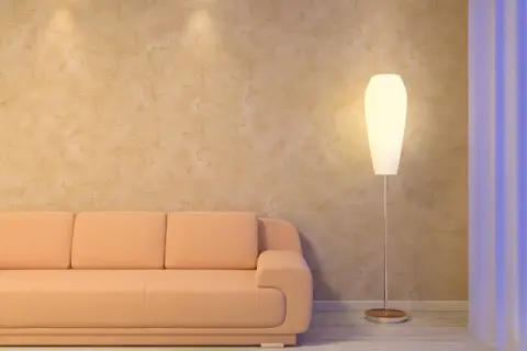 Sofá naranja junto a una lámpara de pie, con una pared de estucado en tonos tierra y cortinas azules al fondo.