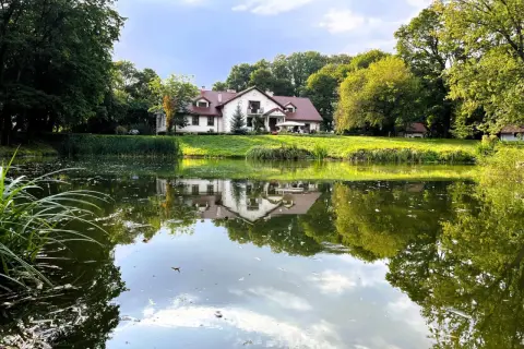 Malowniczy dom seniora w pałacu Jastrzębia Góra, odbijający się w spokojnej tafli stawu, otoczony zielenią.