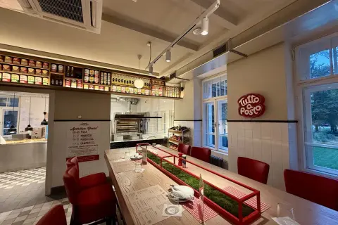 Wnętrze restauracji z czerwonymi krzesłami i długim stołem. Na ścianie wisi neon "Tutto Posto", a nad ladą półki z produktami. Otto Pompieri opinie: warto odwiedzić!