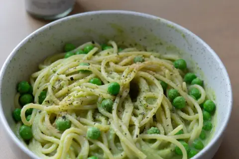Eine Schüssel mit gesunden Nudeln, garniert mit Erbsen und Kräutern, serviert in einer cremigen grünen Sauce.