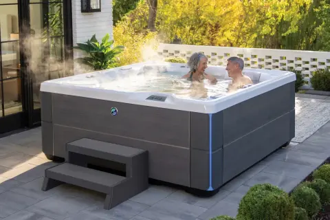 Para relaksu w ogrodzie: para cieszy się gorącą kąpielą w nowoczesnych wannach spa ogrodowych, otoczonych zielenią i słońcem.