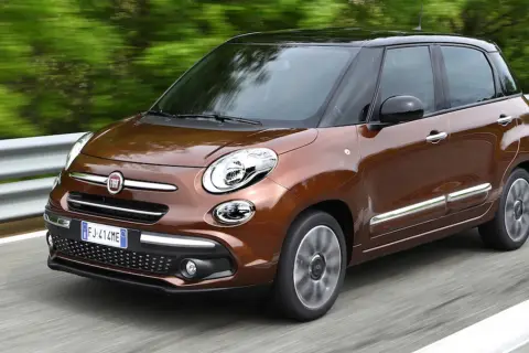 Brązowy Fiat 500L z czarnym dachem pędzi po drodze, otoczony zielenią.